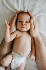 newborn baby making in a diaper, funny face, looking at camera, held by her father.