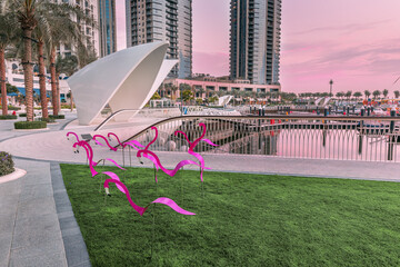 Wall Mural - decorative figurines of pink flamingos on the boardwalk and white arch against the background of the bay with ships and yachts in the marina Creek Harbor in Dubai