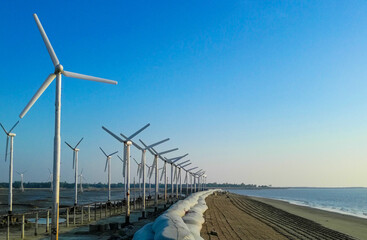 Wall Mural - Row of white windmills on a beach with a blue sky
