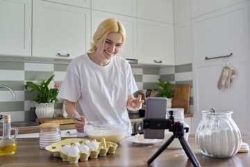 Female teenager learns to cook pancakes, watching video recipe on smartphone