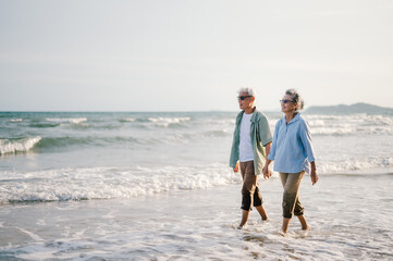 Elderly Asian couple walking on the beach at sunset