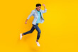 © deagreez - Photo of funny hurrying dark skin guy dressed denim shirt running fast jumping high isolated yellow color background