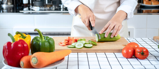 Sticker - Asian housewife wearing apron and using knife to slice cucumber and tomato on chopping board