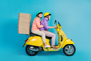 Poster - Portrait of two cheerful elderly retired pensioners riding moped delivering fastfood isolated over bright blue color background