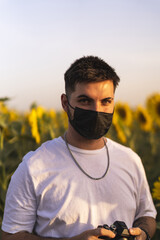 Poster - Vertical shot of a handsome male wearing a face mask and taking photos on a sunflower field