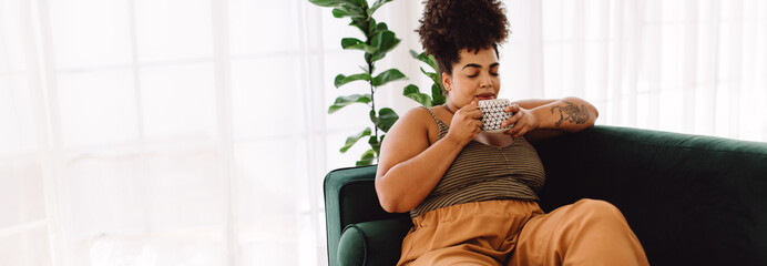 Wall Mural - Woman sitting on sofa and drinking coffee