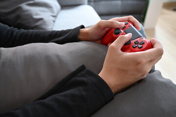 Young man playing video game with joystick while sitting on couch.