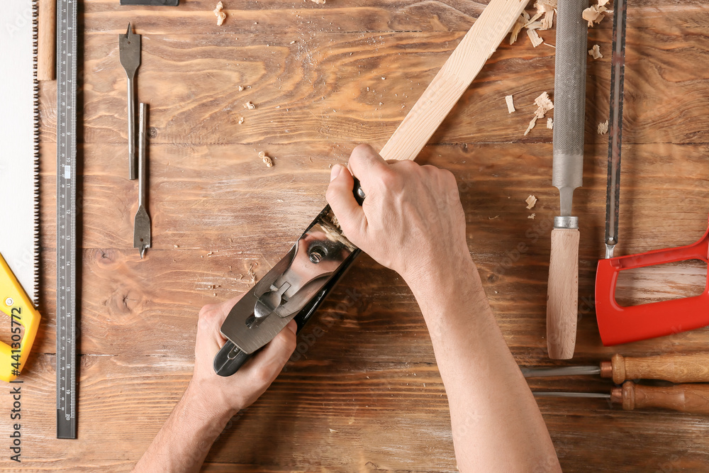 Carpenter planing plank on wooden background