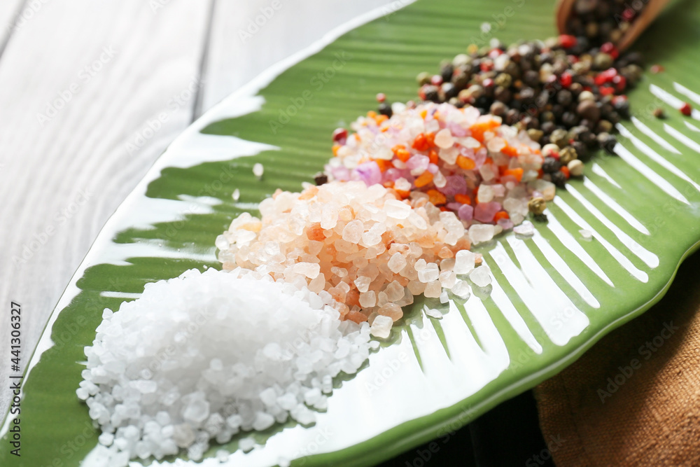 Plate with different salt and peppercorns on table, closeup