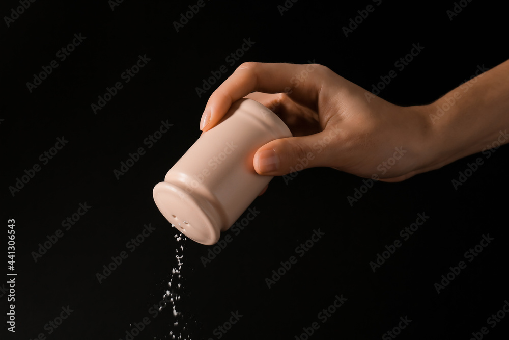 Woman sprinkling salt from shaker on dark background, closeup