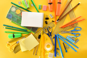 pile of school supplies on yellow background top view