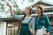 © PR Image Factory - happy two young asian women friends walking outdoors standing by japanese wooden house. ladies looking aside while pointing finger to sky. cheerful female travelers smiling share beautiful scenery