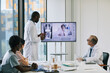 © Seventyfour - Portrait of African-American doctor standing by digital screen in onference room and talking to expert via video call, copy space