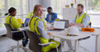 © TommyStockProject - Young woman constructor wearing reflective vest posing at camera sitting at desk in modern office