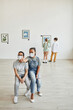 © Seventyfour - Wide angle view at African-American boy and girl looking at paintings in art gallery and wearing masks, copy space