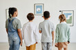 © Seventyfour - Minimal back view at multi-ethnic group of children looking at paintings in modern art gallery and wearing headphones