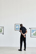© Seventyfour - Minimal full length back view at African-American man looking at paintings in modern art gallery, copy space