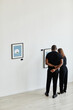 © Seventyfour - Minimal wide angle view at elegant couple looking at paintings in modern art gallery, copy space