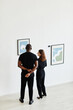 © Seventyfour - Minimal high angle view at elegant couple looking at paintings in modern art gallery, copy space