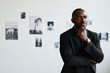 © Seventyfour - Minimal waist up portrait of elegant African-American man wearing black while looking at photographs in modern art gallery, copy space