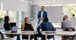 © TommyStockProject - Confident businessman standing near board discussing business strategy with colleagues