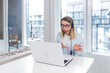 © Liubomir - Young blonde woman with a headset and glasses communicates with customers at a distance in front of a laptop or computer screen in the office of an online consumer support call center. conference help