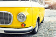 Close-up detail front view of headlight part old vintage bright yellow retro mini bus car van parked in european city center on cobble stone paved road. Fun vehicle for snack delivery sale journey