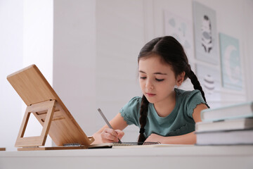 Wall Mural - Little girl doing homework with tablet at table in room