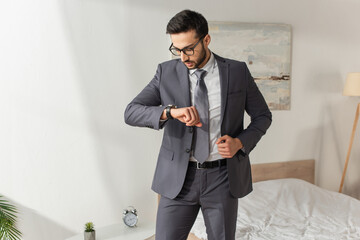 Wall Mural - Businessman in eyeglasses looking at wristwatch in bedroom