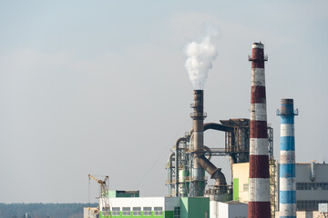 A view of a large factory or enterprise with large smoking chimneys against a blue sky. Environmental pollution by industrial waste. White smoke comes out of the chimney.