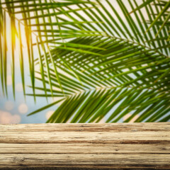 Wall Mural - Wooden rustic table on a hot summer day against a backdrop of green tropical palm trees 