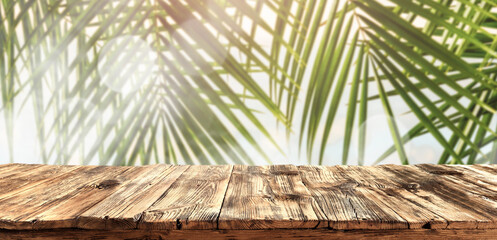 Wall Mural - Wooden rustic table on a hot summer day against a backdrop of green tropical palm trees 