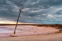 An Old Power Pole Leaning Over On The Edge Of A Salt Lake Under A Gloomy Sky