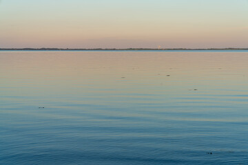 Poster - calm ocean waters at sunset with forest and shoreline in the background