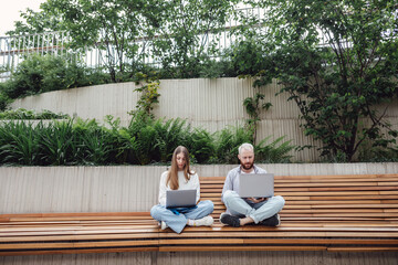 A young students girl and man sits in an urban park in the city and study university disciplines of science. Working with laptops while sitting on a bench. University campus, education in the open air