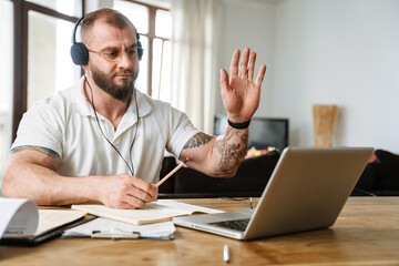 Wall Mural - White man in headphones gesturing while working with laptop at home