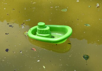 Green toy plastic boat in small pond with green water and plant debris. Pond of the laundry of the village of Armejún, province of Soria, Spain.