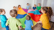 © oksix - Children stretching colorful parachute for fun team games
