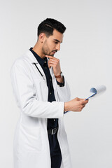 Wall Mural - Side view of pensive muslim doctor looking at diagnosis on clipboard isolated on grey