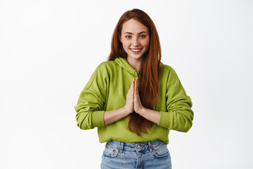 Please. Smiling cute ginger girl hold hands in pray, begging or asking for favour, make namaste gesture, say thank you, standing over white background