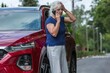 Senior woman leans against her red car and calls for help after causing an accident