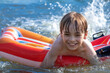 Summer holiday season and vacations at sea. A child boy on an inflatable mattress floats on the water lifting splashes with his feet. Happy face of a teenager