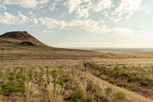 A Lone Cyclist On A Dirt Trail Through A Field Of Shrubs And Brush At The Foot Of A Small Mountain, Petroglyph NM, New Mexico