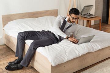 Wall Mural - Businessman with smartphone using laptop on bed at home