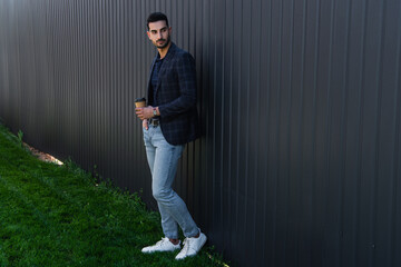 Wall Mural - Young muslim businessman holding coffee to go near fence outdoors