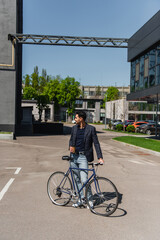 Sticker - Side view of smiling muslim businessman with bike and coffee to go standing on street