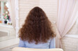 Female back with long curly brunette hair in hairdressing salon