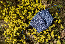 Blue Protective Mask, In Floral Pattern, Lies On Beautiful Yellow Flowers In A Park.