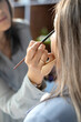 © kostikovanata - Professional female makeup artist applying cosmetics on model face use brush working at beauty salon