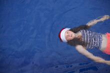 Young Girl Floats In A Pool Wearing A Festive Christmas Santa Hat